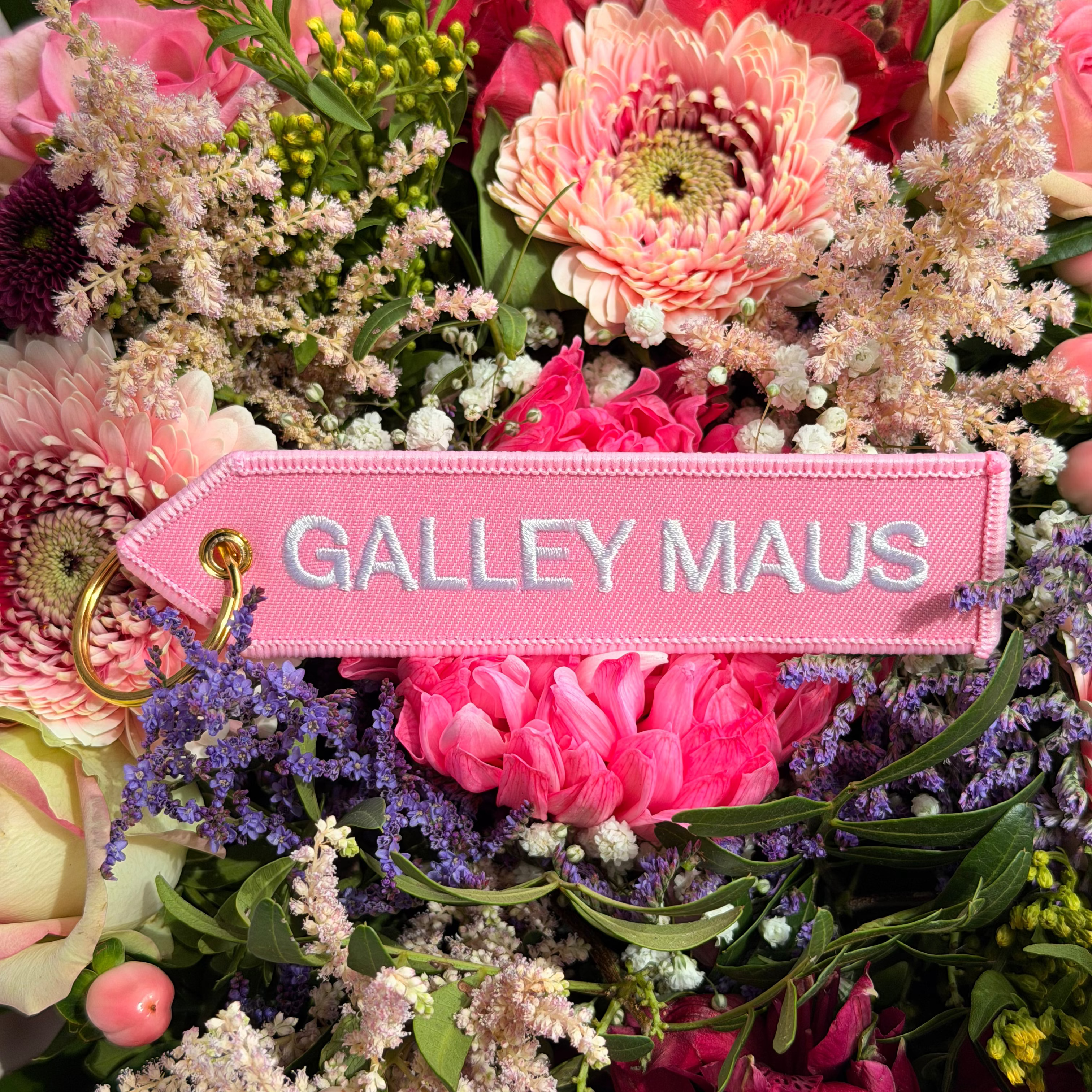 Rosa 'Galley Maus' Schlüsselanhänger mit goldenem Ring vor bunten Blumen